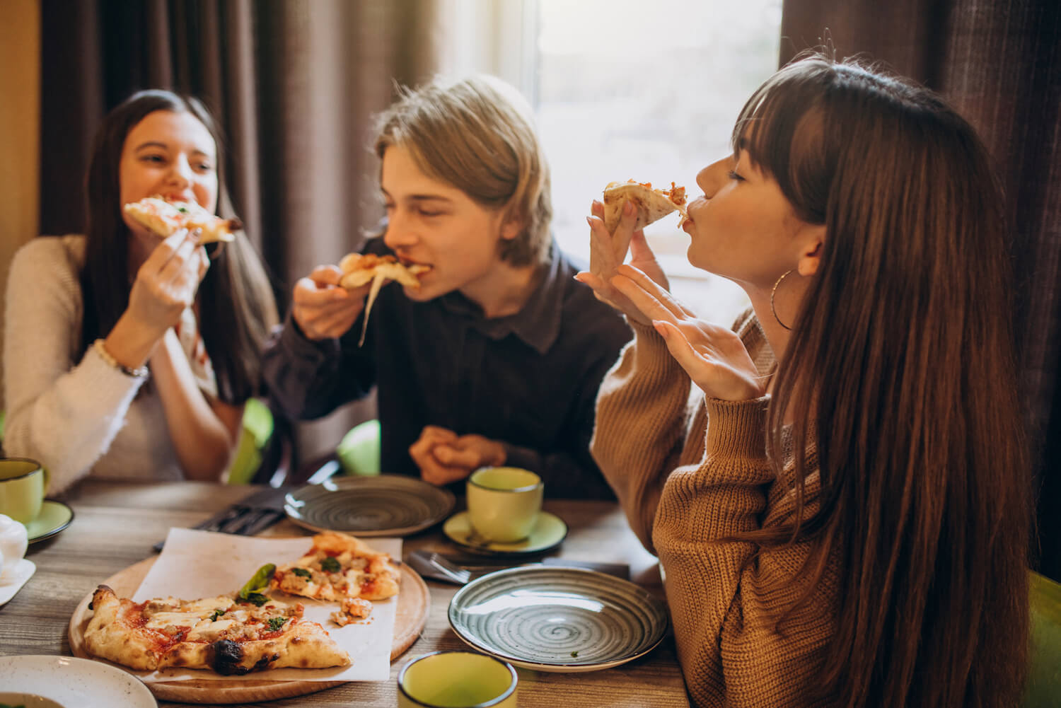 Three friends eating pizza together inside